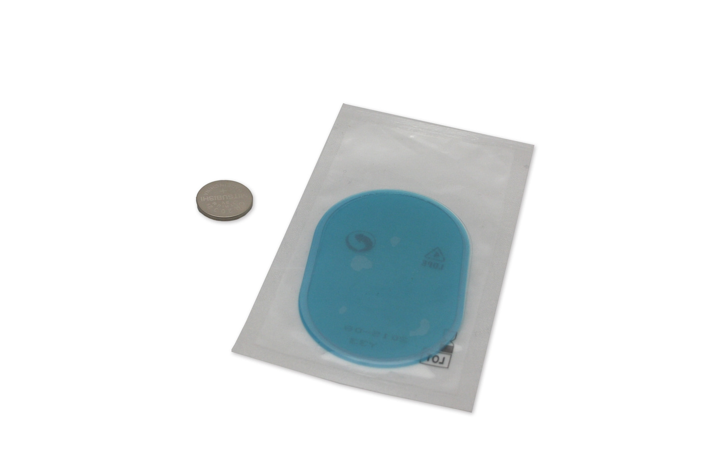 Objeto azul en embalaje junto a una moneda sobre fondo blanco.